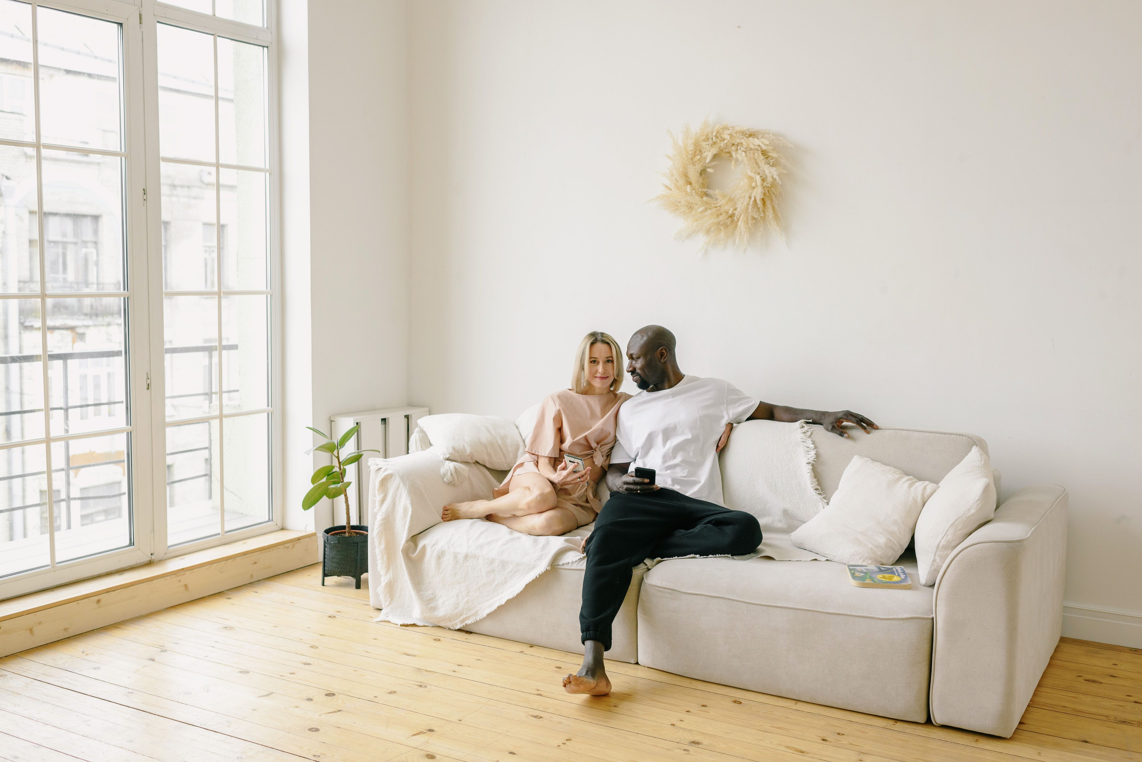 A loving interracial couple sitting on a cozy sofa in a bright, minimalist living room.