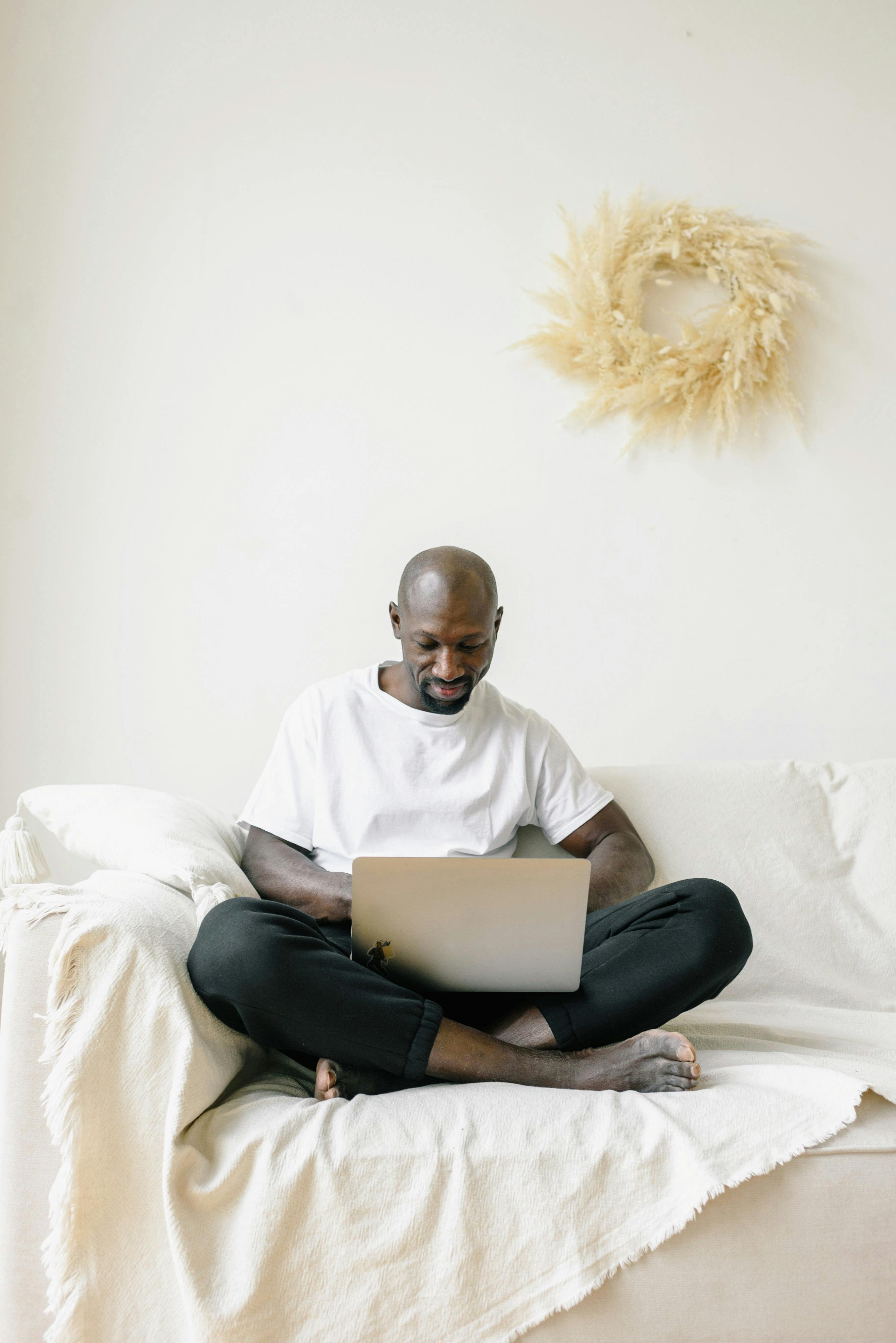 Bald man comfortably working on laptop on a cozy couch at home.