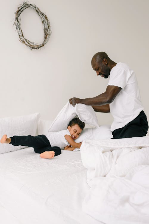 Boy in White Shirt and Black Pants Lying on White Bed