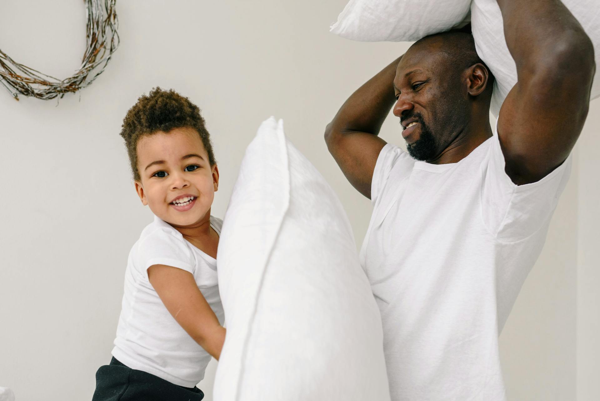 Father and son having fun indoors with a playful pillow fight. Joyful family bonding moment captured.