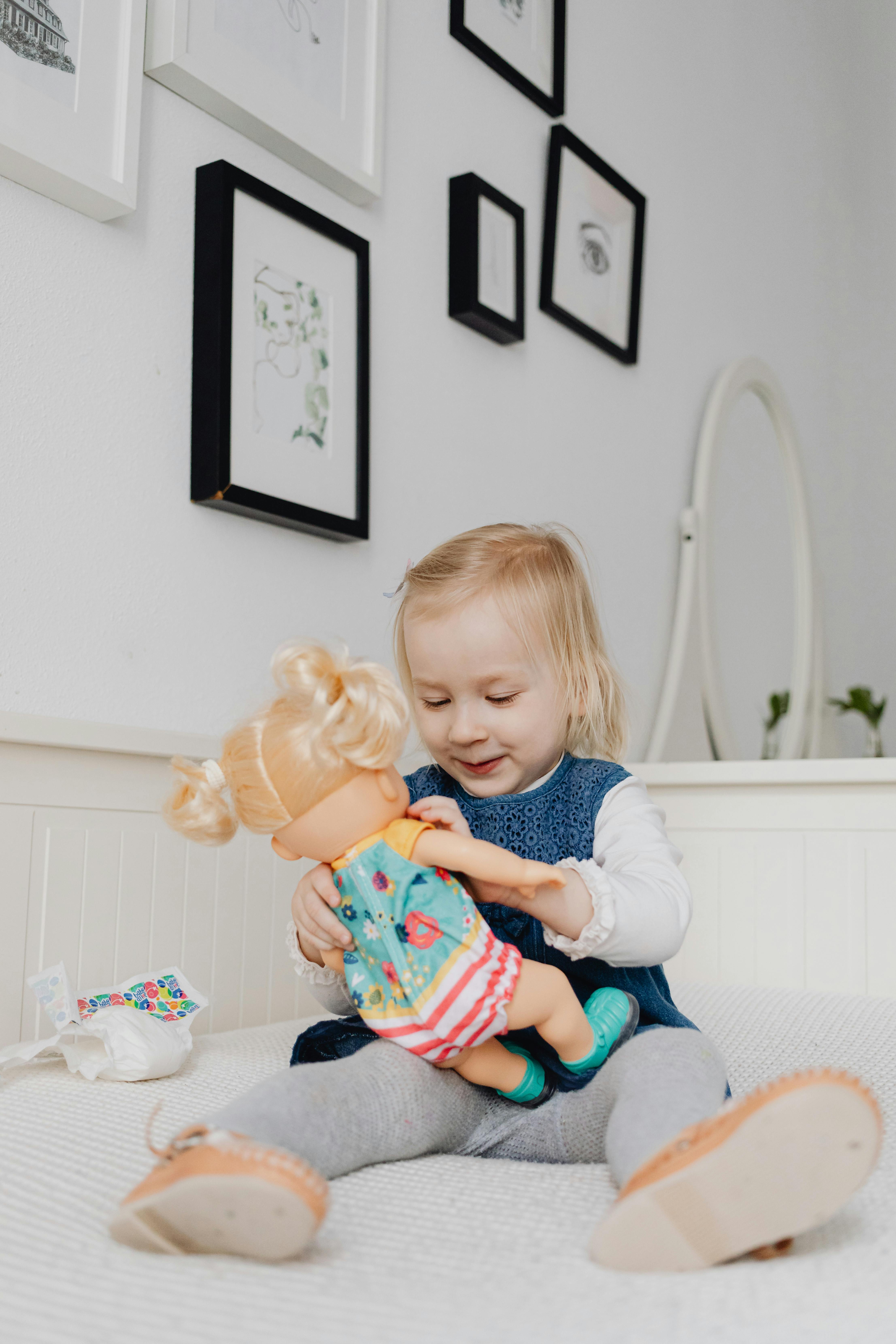 a girl playing a toy doll while sitting on the bed