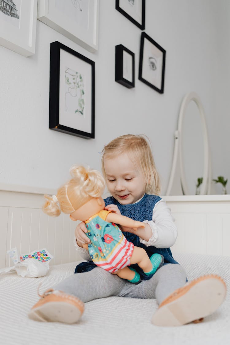 A Girl Playing A Toy Doll While Sitting On The Bed