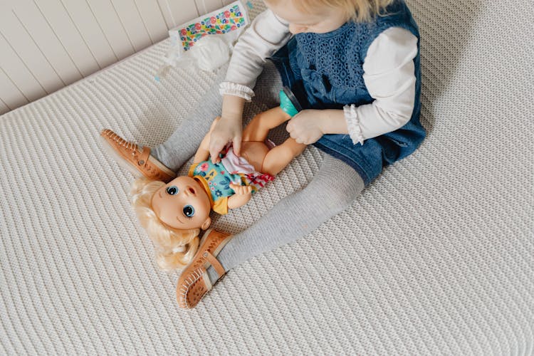 A Child Playing With A Toy Doll On The Bed