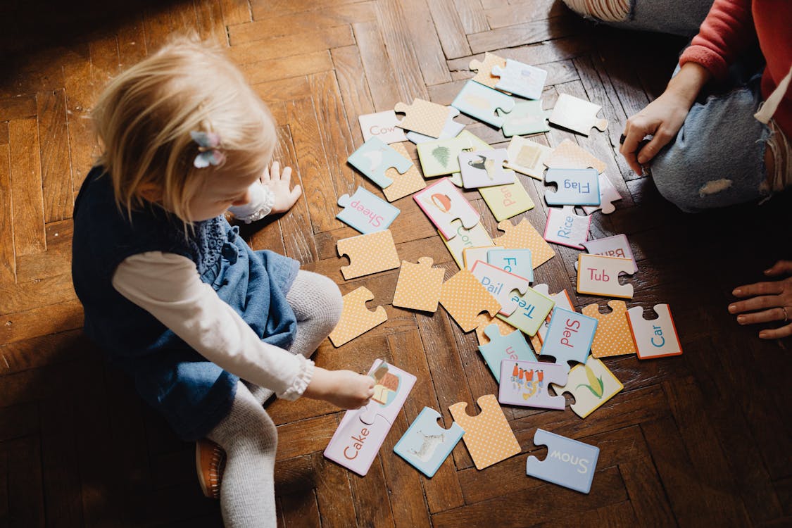 Free Girl Playing Puzzle Game on Brown Wooden Floor Stock Photo