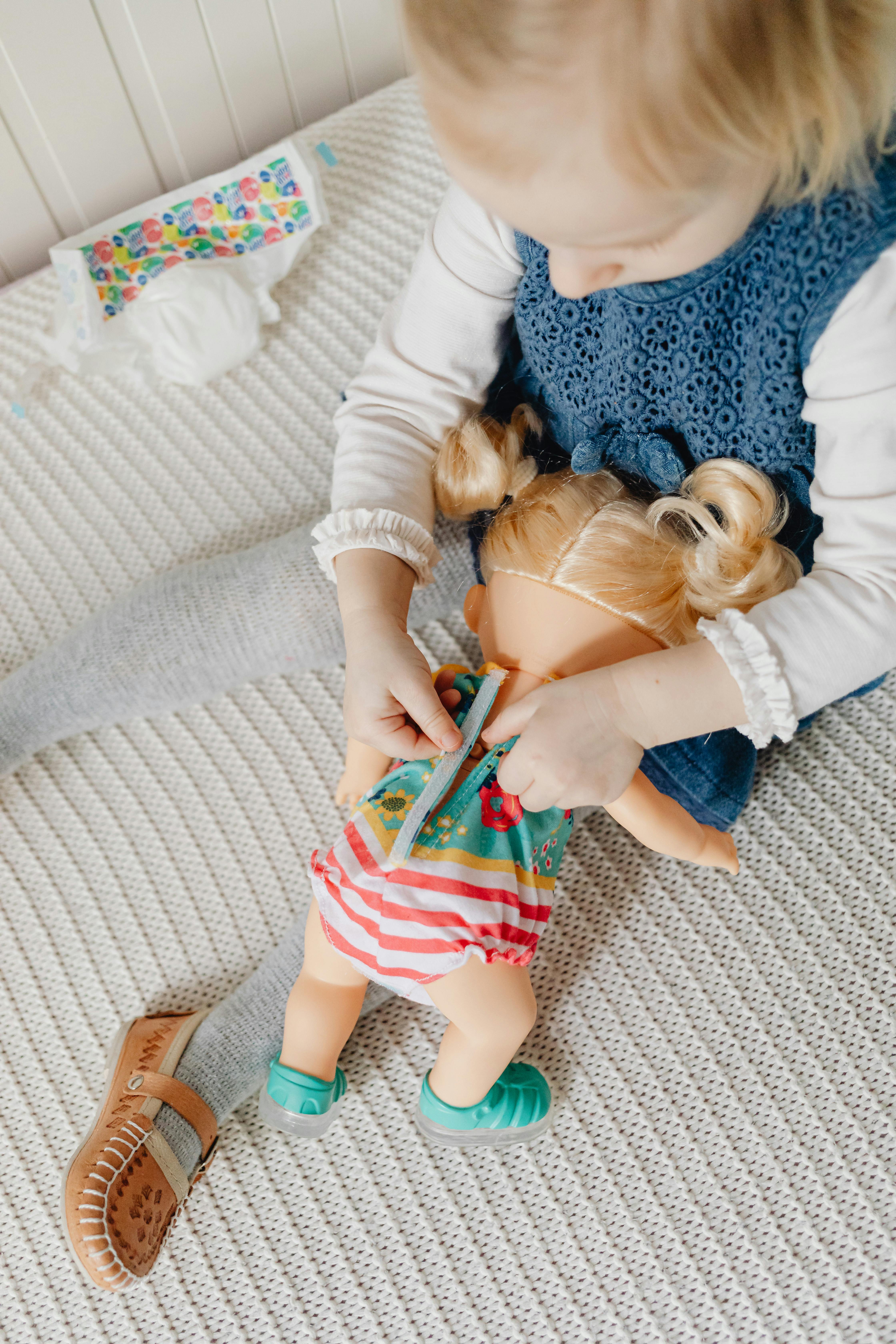 a girl sitting on the bed playing a toy doll