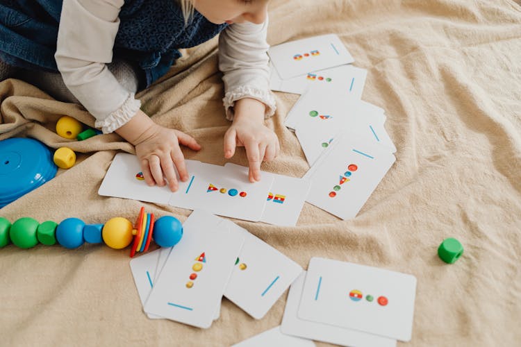 A Toddler Holding Shape Cards On The Blanket