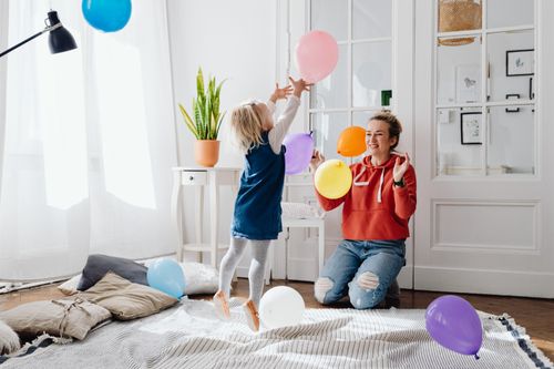 Free Joyful indoor scene of mother and daughter playing with colorful balloons in a cozy room. Stock Photo