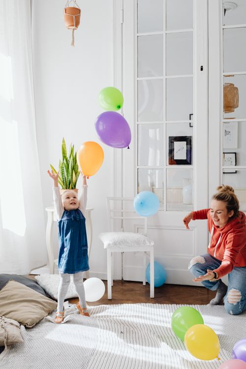 Free A joyful scene of a mother and daughter playing with colorful balloons indoors. Stock Photo