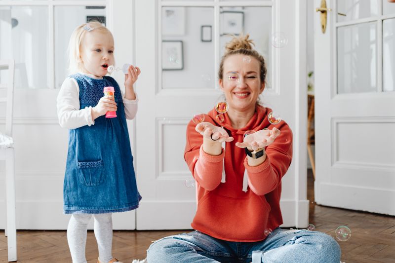 Smiling mother and child playing with bubbles indoors, sharing joyful moments.