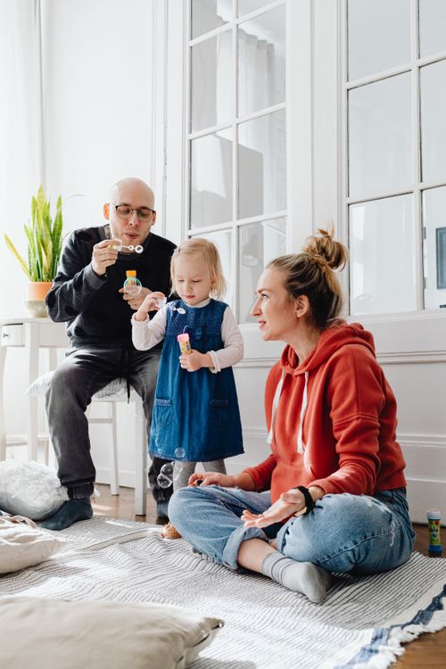 Free A joyful family playing and blowing bubbles on the living room floor. Stock Photo