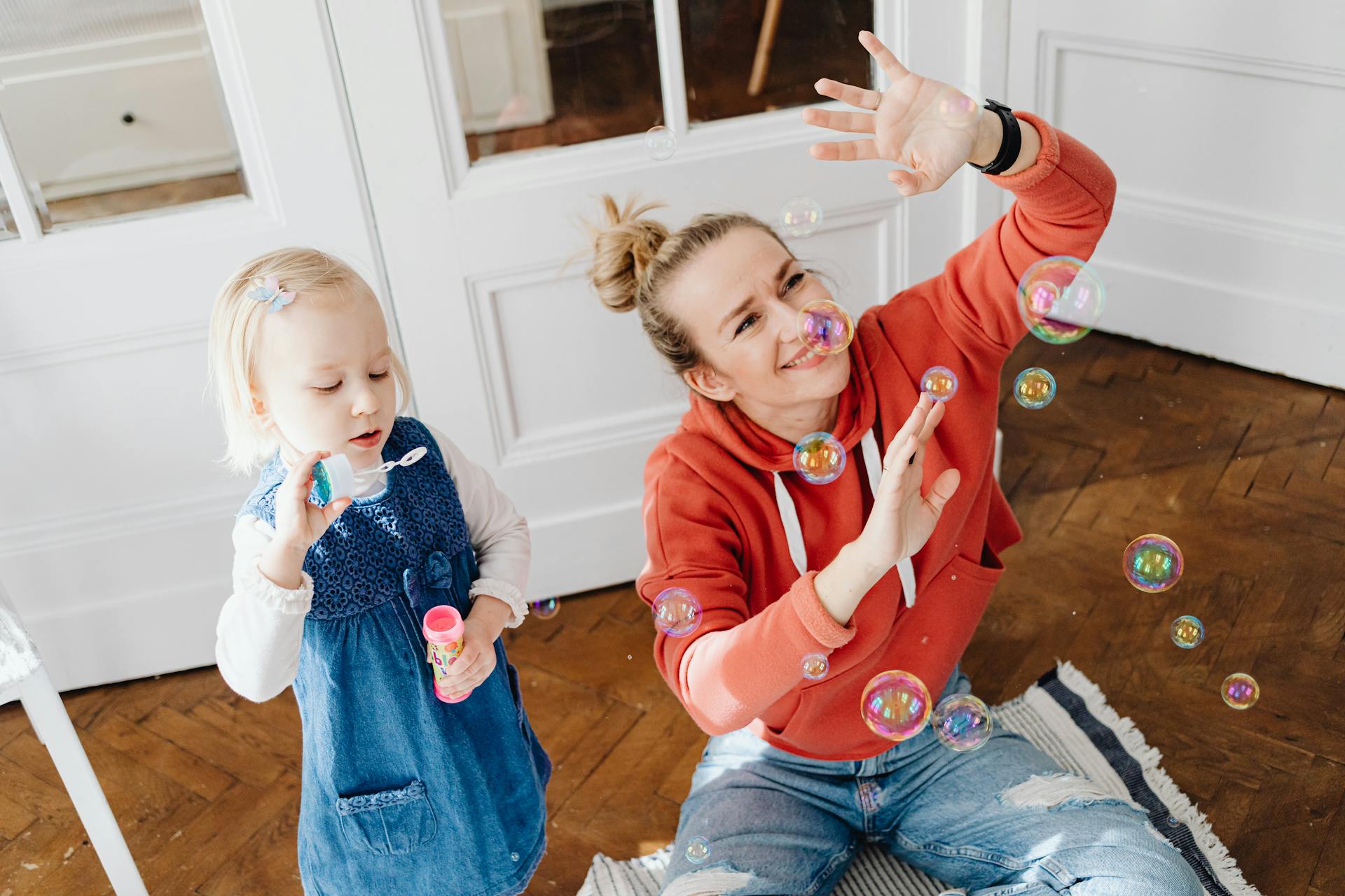 Happy mother and daughter playing with bubbles indoors, enjoying quality time.