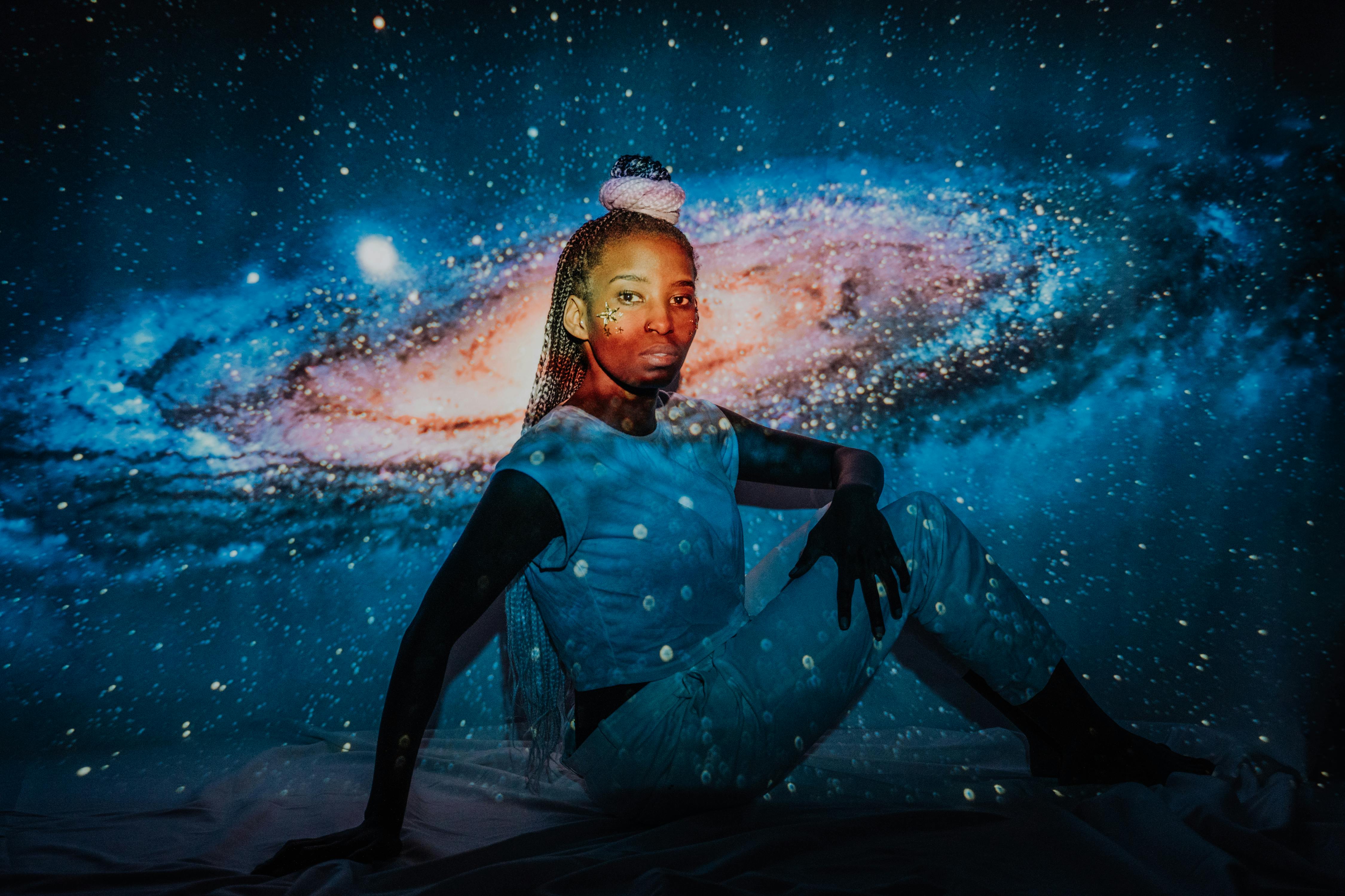 Fashionable woman posing against a galaxy-themed starry background in a studio setting.
