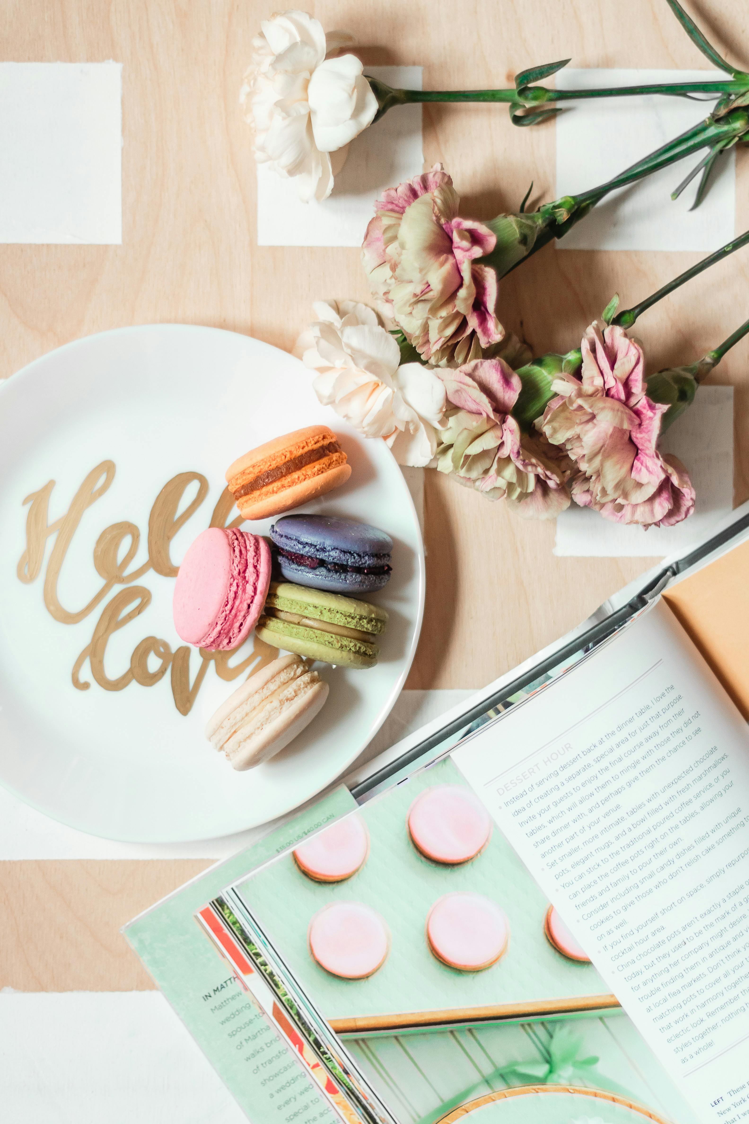 composition of macaroons on plate near magazine and flowers