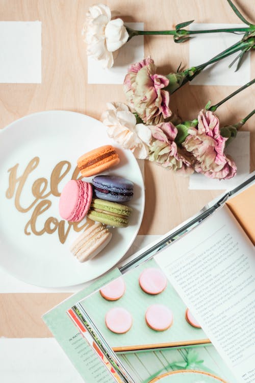 Free Top view arrangement of delicious macaroons on plate on table near opened magazine and tender flowers Stock Photo