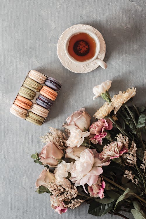Box with macaroons near tea cup and bouquet of flowers