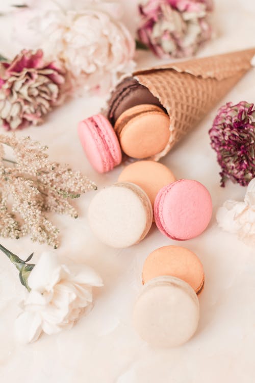 Waffle cone with macaroons near flowers on table