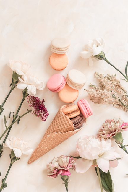 Aesthetic flat lay featuring brightly colored macarons in a waffle cone surrounded by delicate flowers.