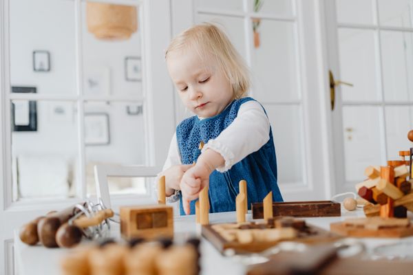Blonde toddler focused on assembling wooden toys