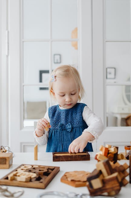 A toddler girl focused on playing with wooden blocks indoors, wearing a blue dress.