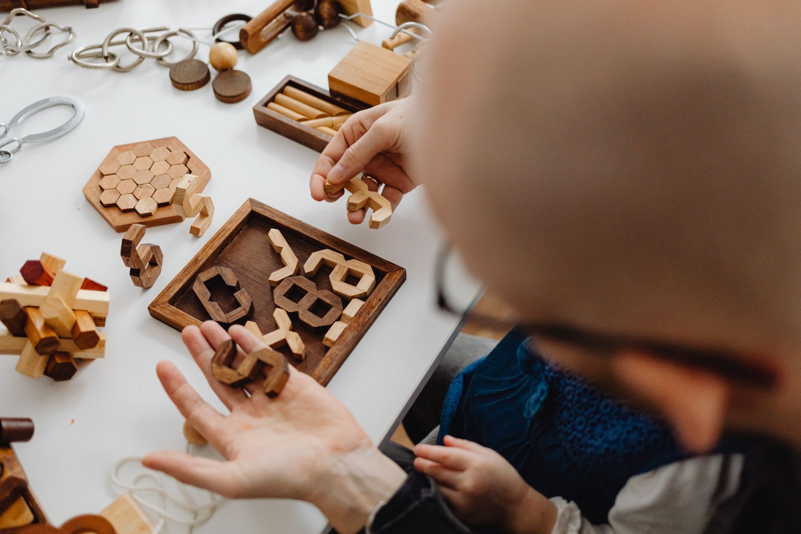 Adults and children handling wooden brain teasers together on a white tabletop