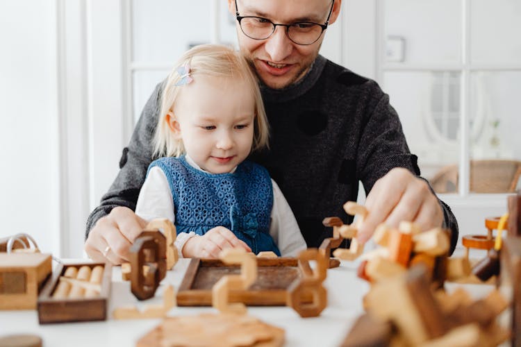 A Man Talking To His Daughter While Playing Wooden Toys On The Table