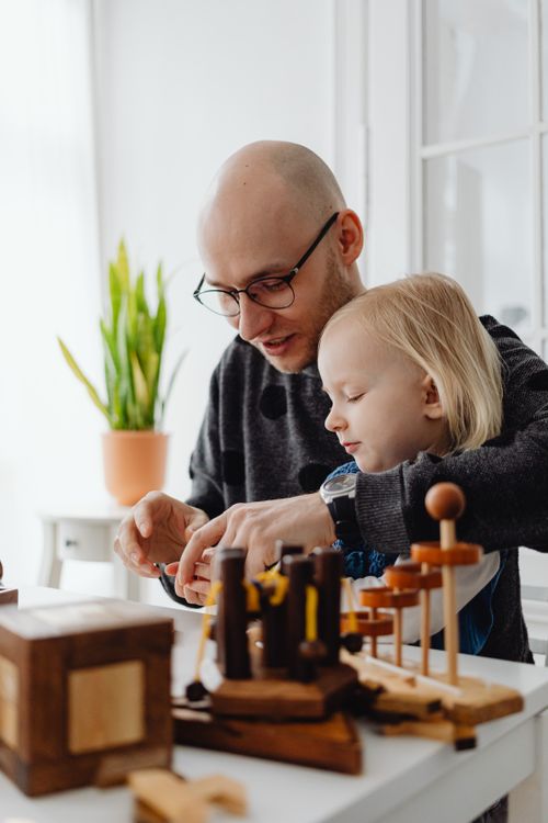 Free A father and daughter engage in creative play with wooden toys indoors, fostering bonding and learning. Stock Photo