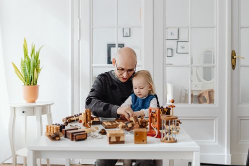 Free Father and young daughter sitting at a table playing with wooden toys in a bright room. Stock Photo
