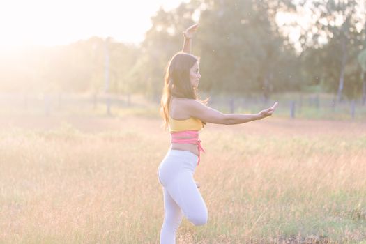Side view of woman performing yoga in a sunlit field, embodying balance and mindfulness.