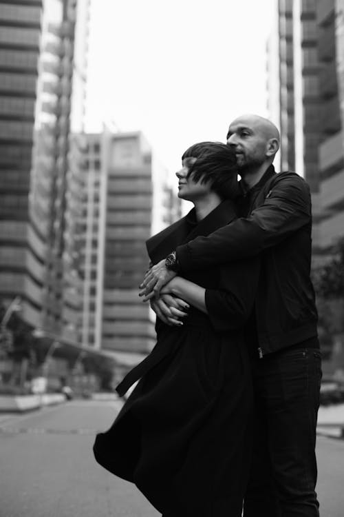 Grayscale Photo of a Bald Man Hugging a Woman 