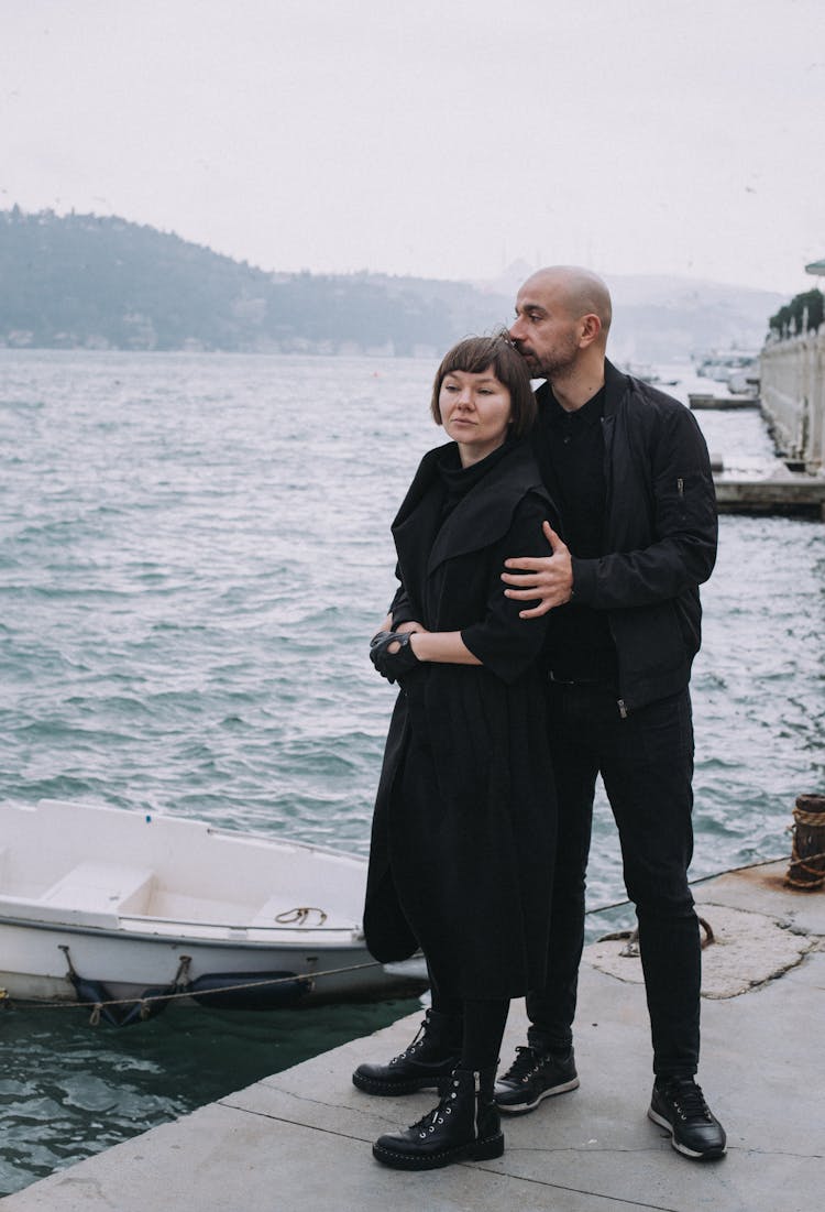 A Couple In Black Outfit Standing On A Dock