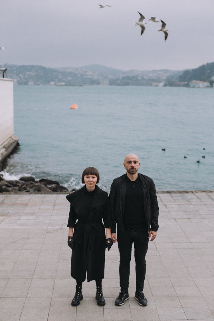 Man In Black Jacket Standing Beside Woman In Black Dress