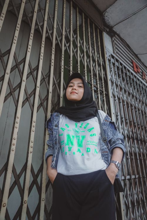 Free Woman in denim jacket and hijab stands confidently with hands in pockets. Stock Photo