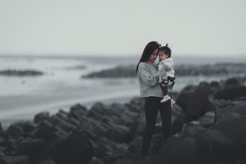 A Woman in Gray Sweater and Black Pants Standing while Carrying Her Baby