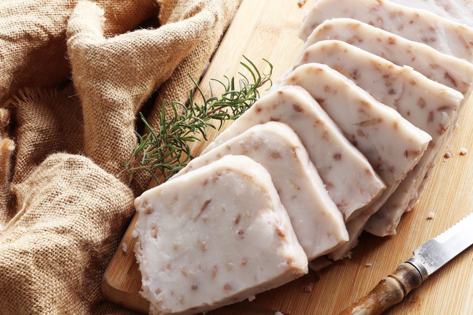 Thin slices of head cheese showing chunks of pork and herbs suspended in translucent aspic, served with mustard and rye bread