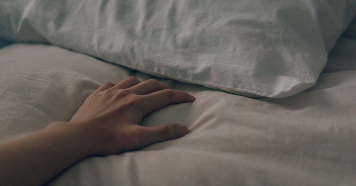 Hand bij een hoofdkussen op bed