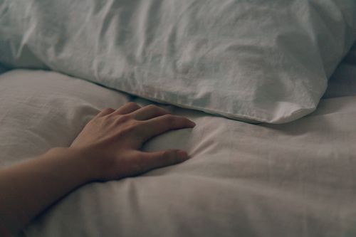 Free A gentle hand rests on a soft pillow and bed sheet, capturing a serene bedroom scene. Stock Photo