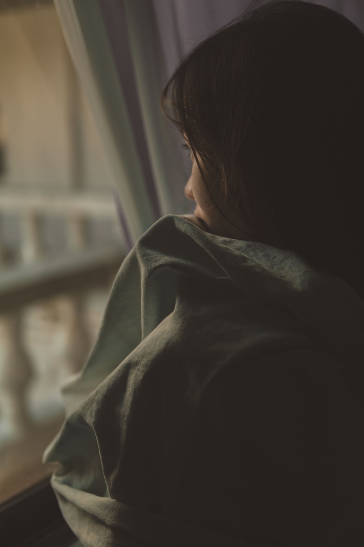 A young woman sitting by a window in soft natural light, pensive and withdrawn — the quiet, unexplainable feeling that something was wrong