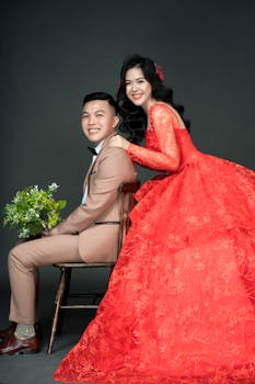 Stylish Asian couple posing joyfully in red wedding attire in a studio setting.