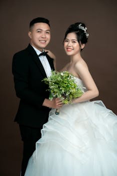 Smiling Asian couple in wedding attire posing gracefully in studio.