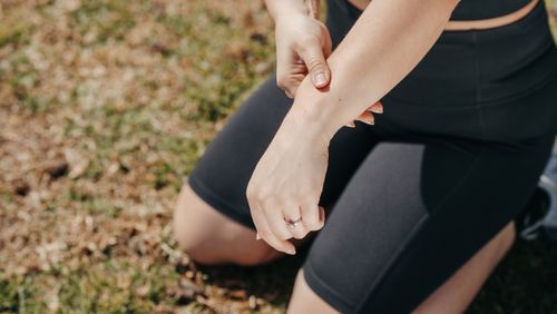 Free Close-up of a person kneeling outdoors while checking their arm in active wear. Stock Photo