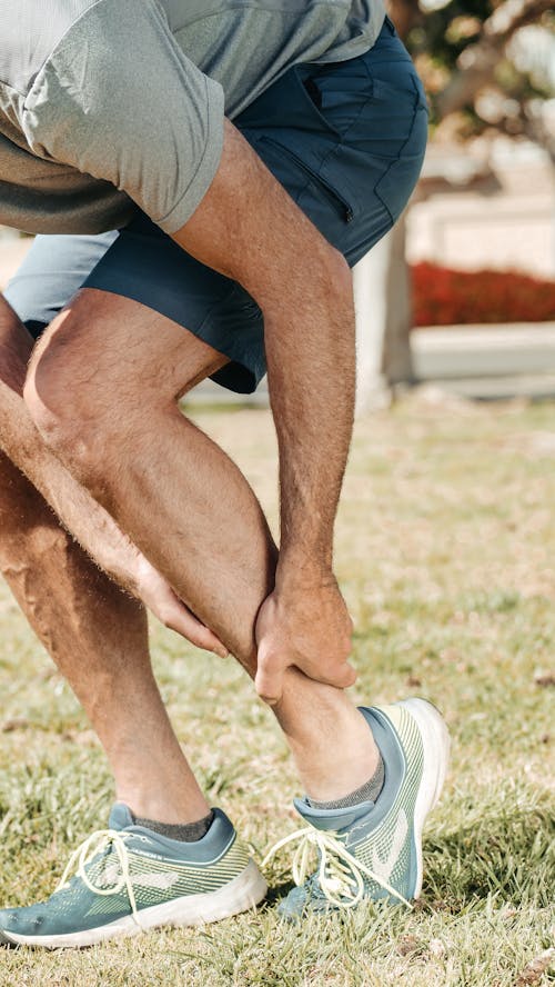Free Adult male grabbing ankle due to injury in outdoor setting, wearing rubber running shoes. Stock Photo