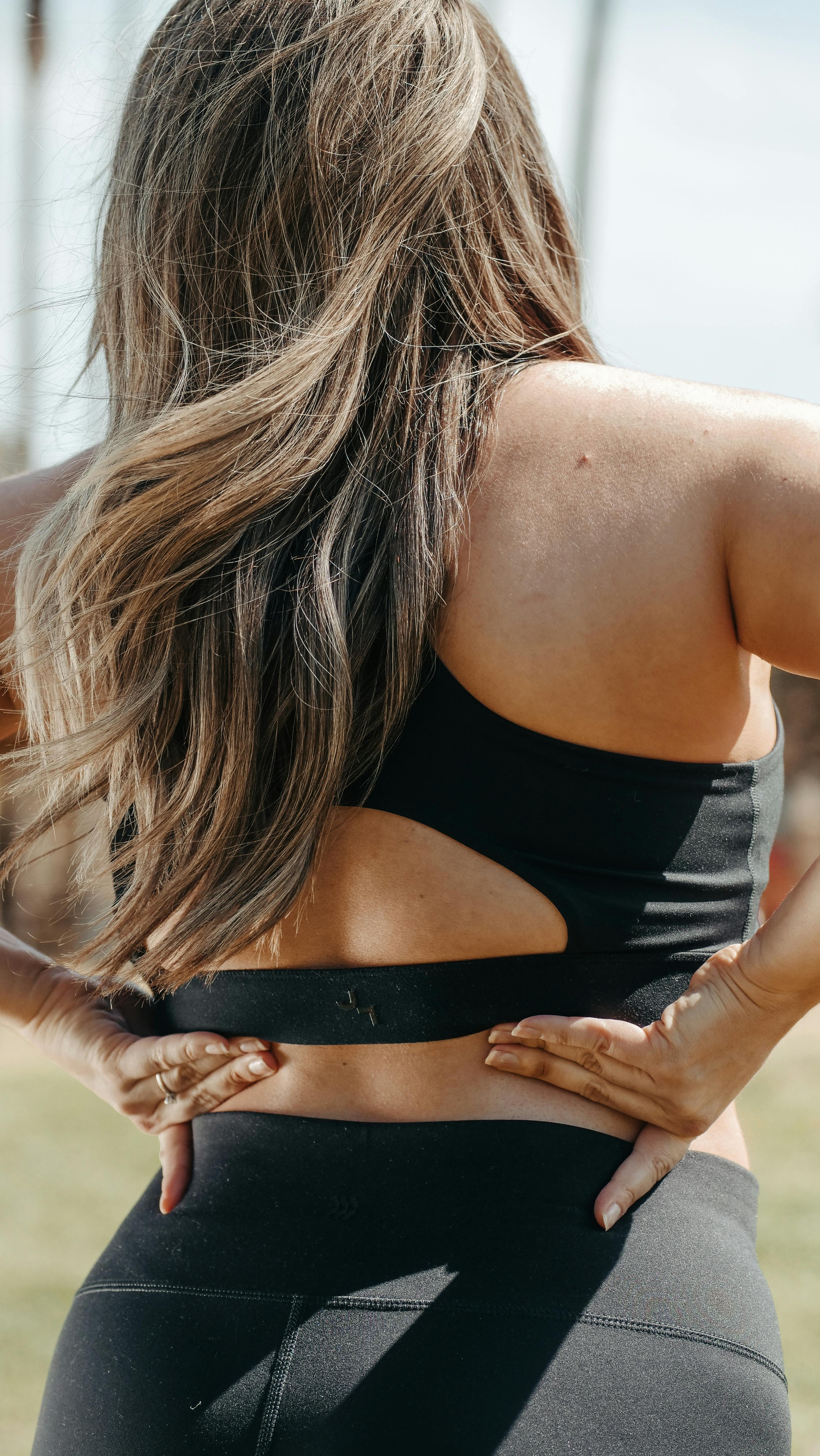 Back view of a woman in activewear holding her waist outdoors, capturing a moment of focus and energy.