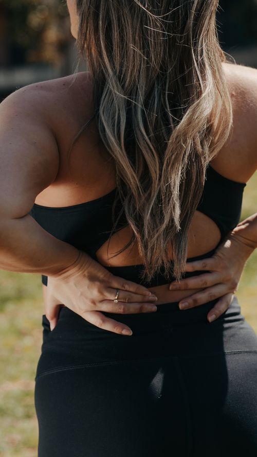 Free A woman in activewear stretching her back outdoors in a sunlit park setting. Stock Photo