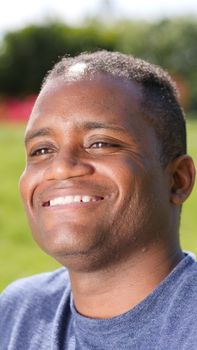 Close-up portrait of a smiling man basking in sunlight with natural background.