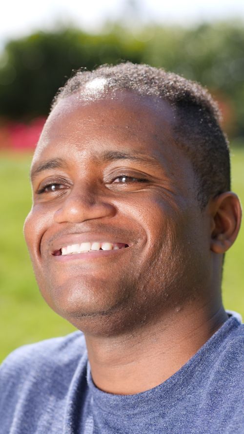 Free Close-up portrait of a smiling man basking in sunlight with natural background. Stock Photo