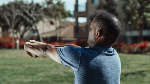 Free Man stretches in a park surrounded by greenery, captured in natural lighting. Stock Photo