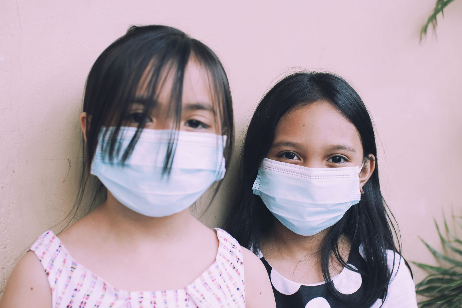 Two girls wearing protective masks for safety and prevention indoors.