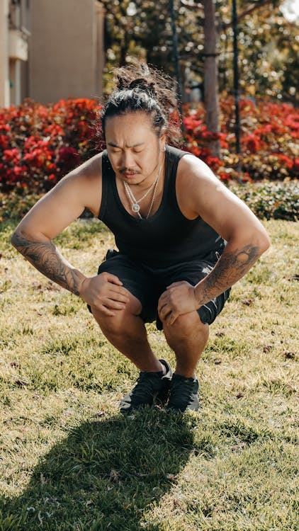 Free Man in Black Tank Top and Shorts Squatting on Grass Stock Photo