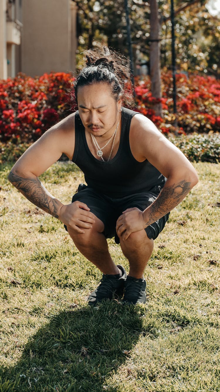 Man In Black Tank Top And Shorts Squatting On Grass