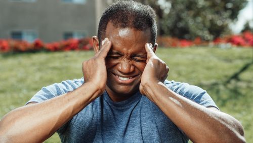 Free African American man massaging his temples outdoors, showing stress and emotion. Stock Photo